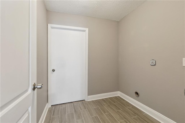 laundry area with a textured ceiling, electric dryer hookup, wood tiled floor, baseboards, and laundry area