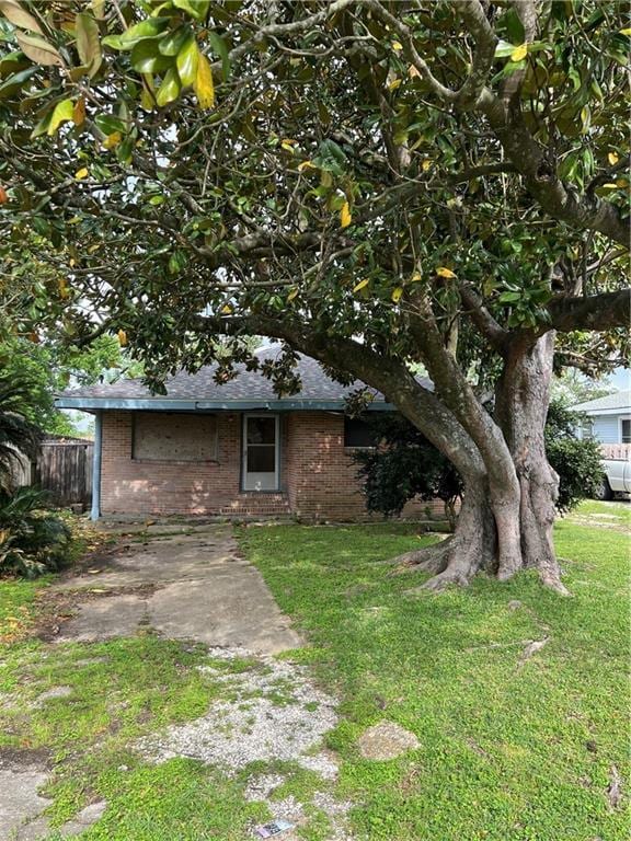 view of front of home with fence, roof with shingles, a front lawn, and brick siding