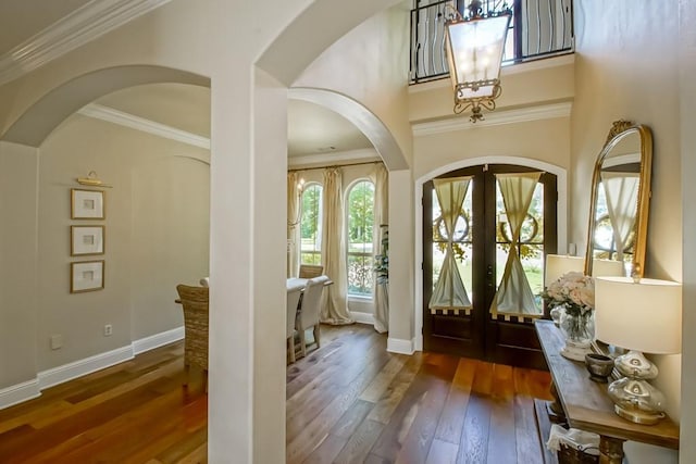 entrance foyer featuring crown molding, wood-type flooring, arched walkways, french doors, and baseboards