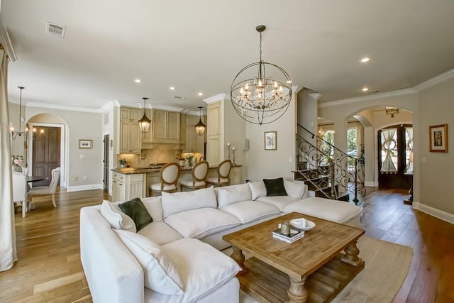 living room with crown molding, arched walkways, visible vents, and a chandelier