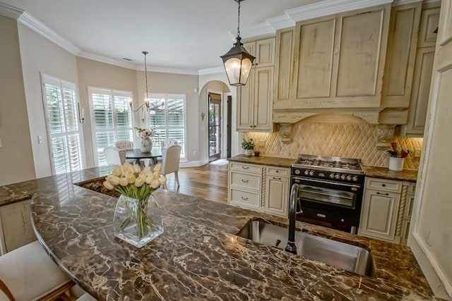 kitchen featuring decorative backsplash, arched walkways, cream cabinetry, a sink, and high end range