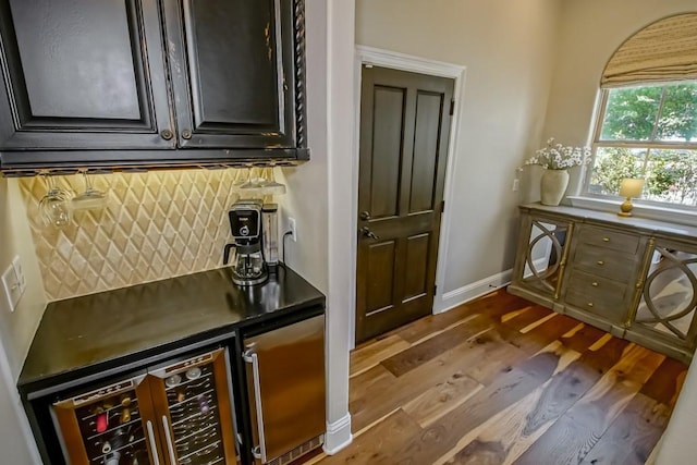 bar with backsplash, dark wood finished floors, baseboards, a bar, and beverage cooler