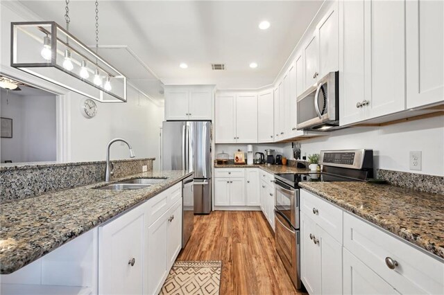 3301 Loyola Ave, New Orleans, LA 70115 - kitchen with visible vents, white cabinetry, a sink, light wood finished floors, and stainless steel appliances