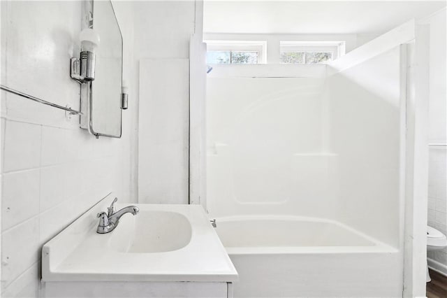full bath with toilet, tile walls, and vanity