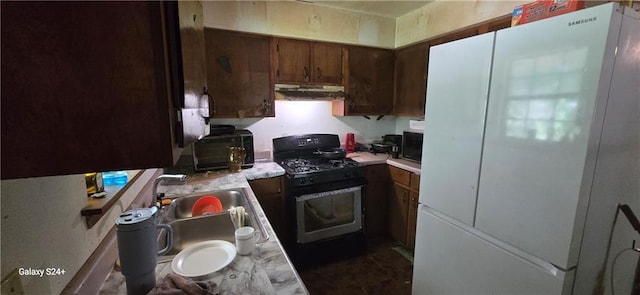 kitchen featuring freestanding refrigerator, black microwave, gas range, light countertops, and under cabinet range hood