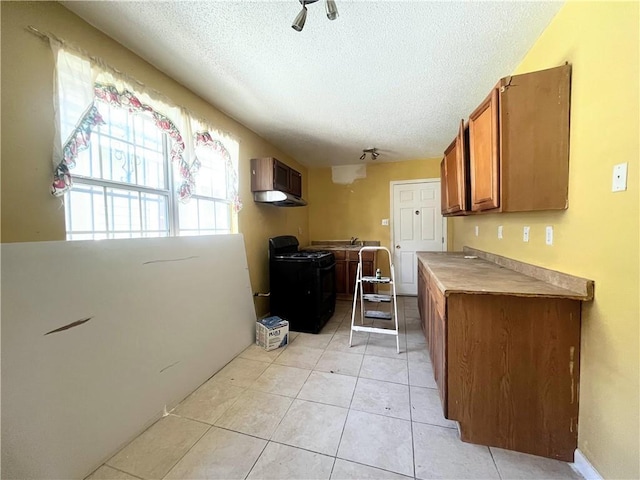2221 Annette St, New Orleans, LA 70119 - kitchen featuring brown cabinets, wall chimney range hood, gas stove, a textured ceiling, and light tile patterned floors