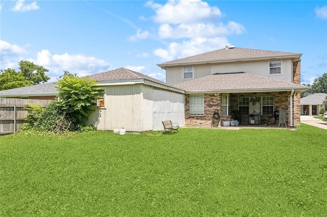 back of property with a lawn, a shingled roof, fence, and brick siding