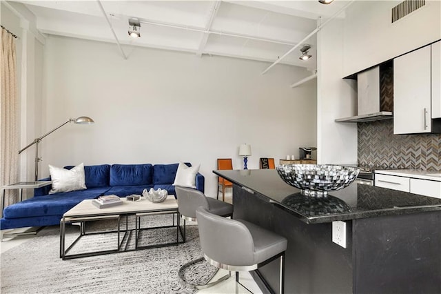 835 Julia St Unit 17, New Orleans, LA 70113 - kitchen featuring wall chimney range hood, white cabinets, a breakfast bar, tasteful backsplash, and visible vents