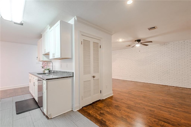 kitchen featuring a sink, brick wall, a ceiling fan, white cabinetry, and visible vents