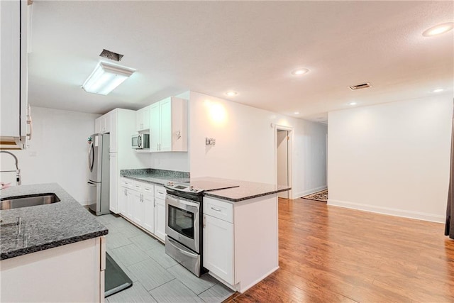kitchen featuring visible vents, appliances with stainless steel finishes, a sink, white cabinets, and dark stone countertops