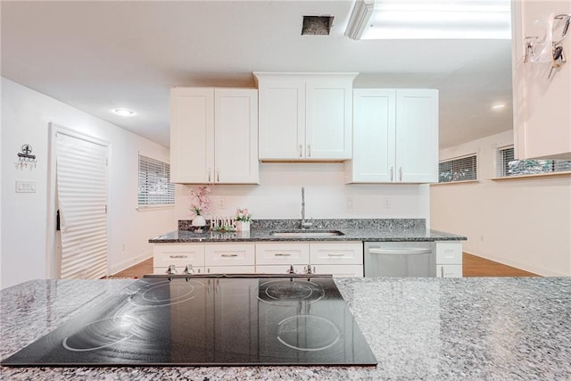 kitchen with baseboards, white cabinets, stovetop, a sink, and dishwasher