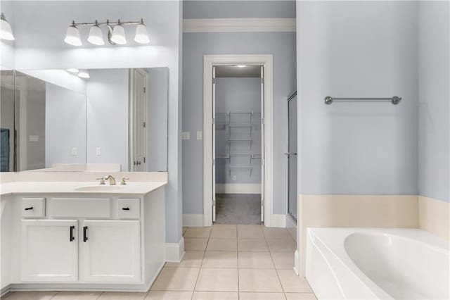 full bath with vanity, ornamental molding, a garden tub, baseboards, and a walk in closet