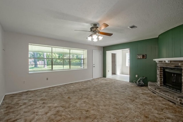 unfurnished living room with ceiling fan, a textured ceiling, visible vents, a brick fireplace, and carpet