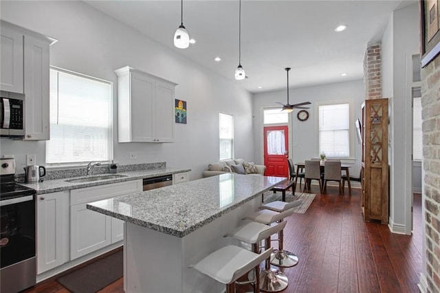 2430 Clara St, New Orleans, LA 70113 - kitchen featuring appliances with stainless steel finishes, ceiling fan, a kitchen island, dark wood-type flooring, and light stone counters