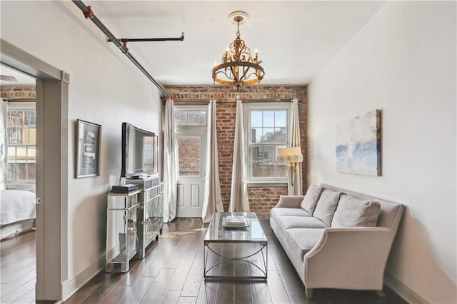 sitting room with baseboards, a chandelier, dark wood-style floors, and brick wall