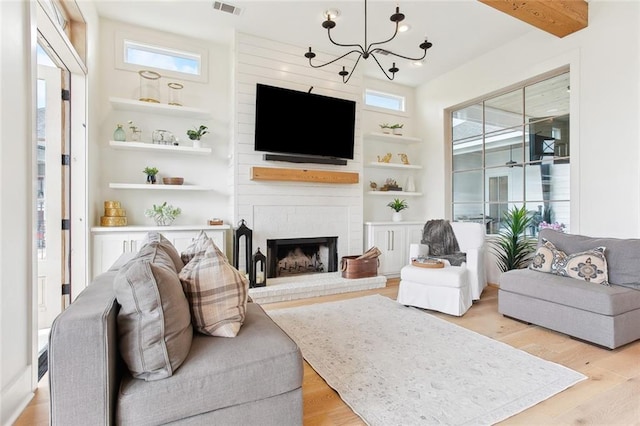 living room featuring light wood-type flooring, a brick fireplace, a notable chandelier, and built in shelves