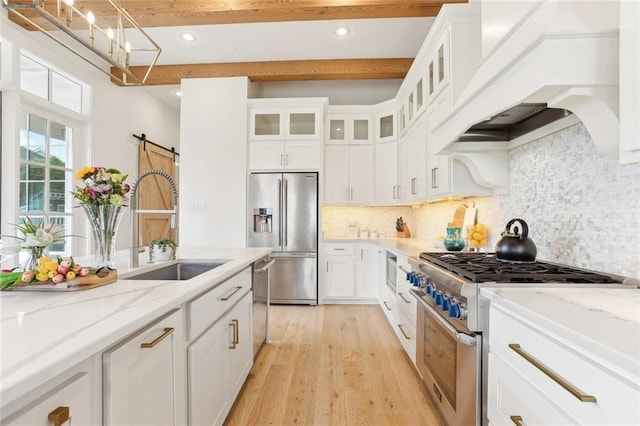 kitchen with high end appliances, custom exhaust hood, beam ceiling, light wood-style floors, and a sink