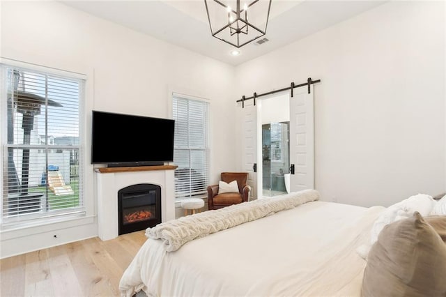 bedroom with a barn door, multiple windows, a glass covered fireplace, wood finished floors, and visible vents