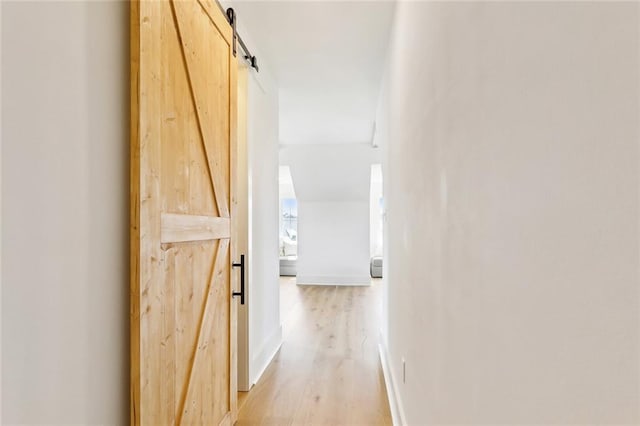 hall with light wood-style floors, baseboards, and a barn door