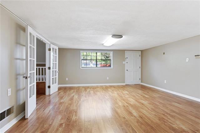 spare room featuring french doors, light wood-style floors, and baseboards