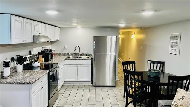 kitchen featuring white cabinets, appliances with stainless steel finishes, light stone counters, a sink, and under cabinet range hood