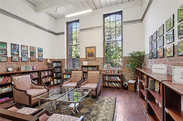 sitting room featuring wood ceiling, a towering ceiling, wood finished floors, and brick wall