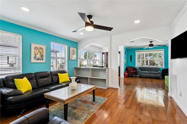 living room featuring a ceiling fan, arched walkways, ornamental molding, and a healthy amount of sunlight