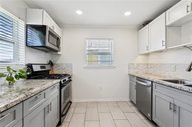 kitchen featuring stainless steel appliances, ornamental molding, decorative backsplash, and a sink