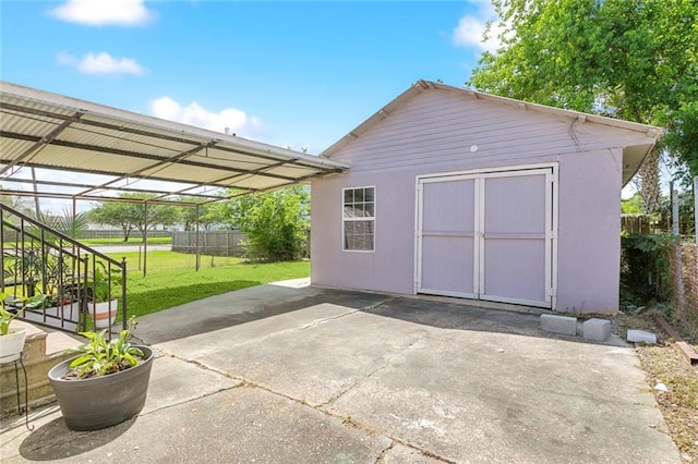 view of outdoor structure with fence, an outbuilding, stairs, and a carport