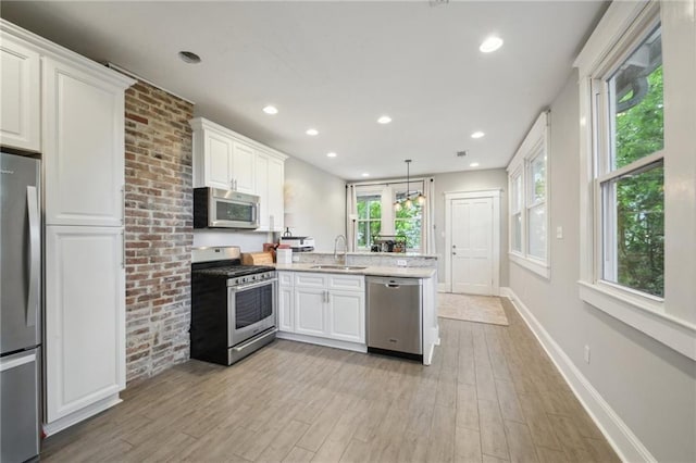 kitchen featuring appliances with stainless steel finishes, a sink, a peninsula, light wood-style floors, and white cabinetry