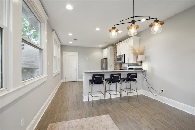 kitchen featuring white cabinets, a kitchen breakfast bar, stainless steel appliances, baseboards, and wood finished floors