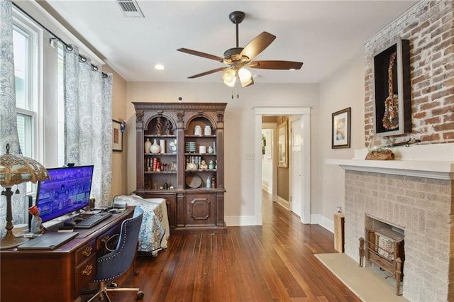 office with ceiling fan, visible vents, a brick fireplace, baseboards, and dark wood-type flooring