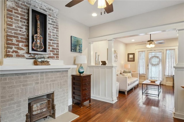 interior space featuring decorative columns, a ceiling fan, a brick fireplace, baseboards, and wood-type flooring