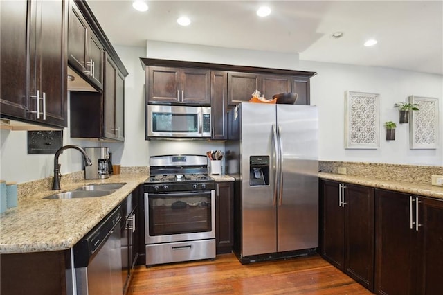 kitchen with dark brown cabinetry, dark wood-type flooring, light stone counters, a sink, and stainless steel appliances