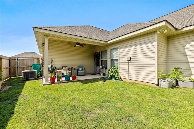rear view of house with ceiling fan, fence, a patio, roof with shingles, and a lawn