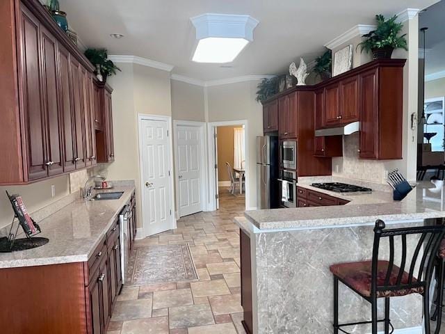 kitchen with appliances with stainless steel finishes, a sink, stone finish floor, a peninsula, and under cabinet range hood