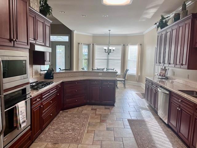 kitchen featuring appliances with stainless steel finishes, light countertops, a notable chandelier, ornamental molding, and stone tile floors