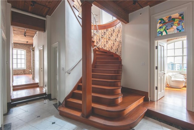 staircase with wooden ceiling, beamed ceiling, tile patterned floors, and brick wall