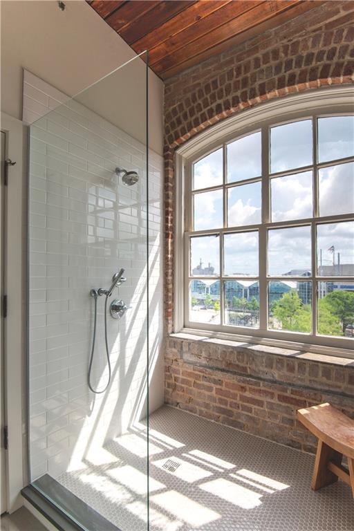 bathroom featuring brick wall, a tile shower, and wooden ceiling