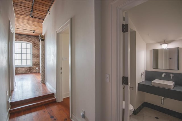 hallway featuring baseboards, a sink, brick wall, and hardwood / wood-style floors