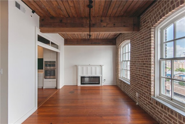 unfurnished living room with brick wall, beam ceiling, wood finished floors, wooden ceiling, and a glass covered fireplace