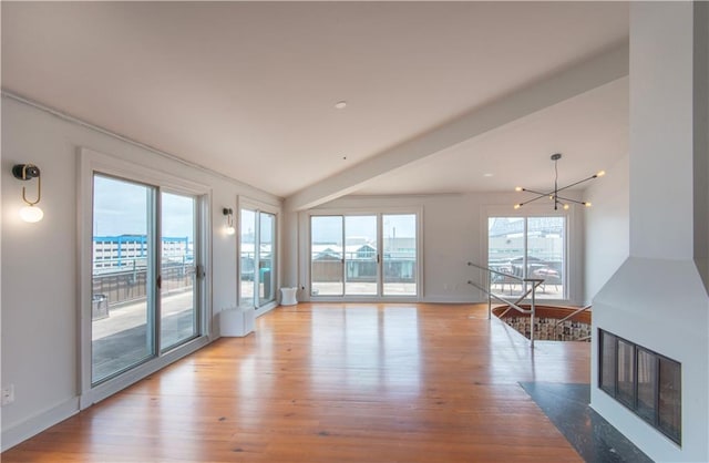 unfurnished living room with baseboards, an inviting chandelier, and light wood finished floors
