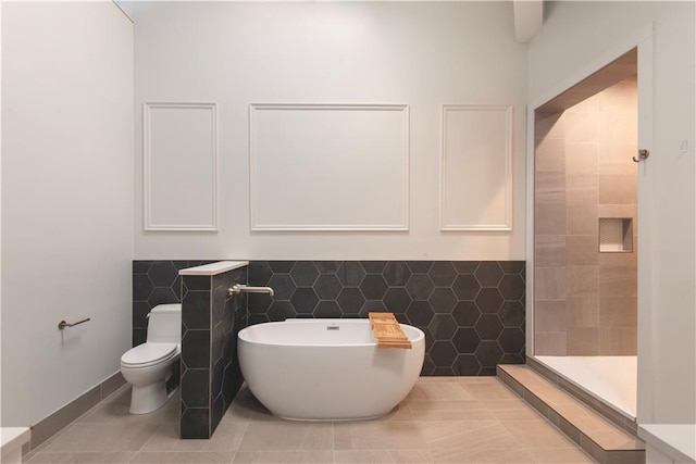 bathroom featuring tile patterned flooring, toilet, tile walls, tiled shower, and a soaking tub