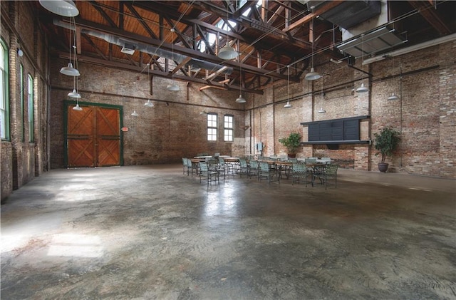 miscellaneous room featuring a garage, a high ceiling, concrete floors, and brick wall