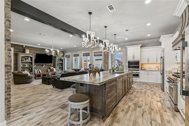 kitchen with visible vents, a sink, open floor plan, an inviting chandelier, and premium appliances