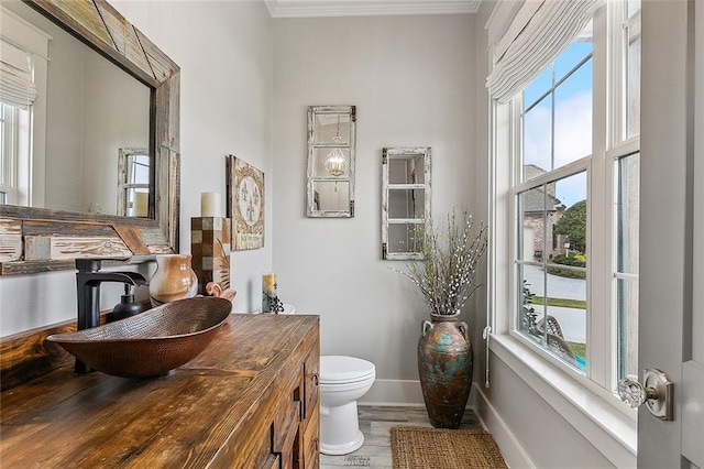 bathroom with toilet, baseboards, ornamental molding, and a healthy amount of sunlight