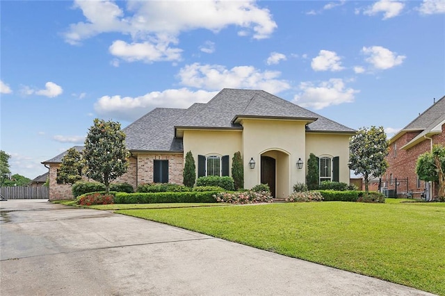 french provincial home with fence, a front lawn, brick siding, stucco siding, and concrete driveway