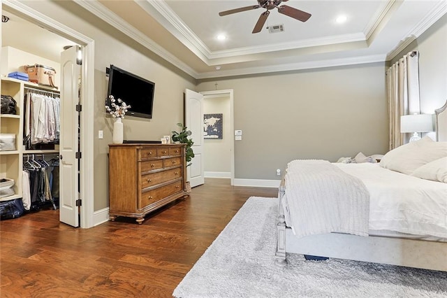 bedroom featuring visible vents, crown molding, a spacious closet, a tray ceiling, and dark wood-type flooring