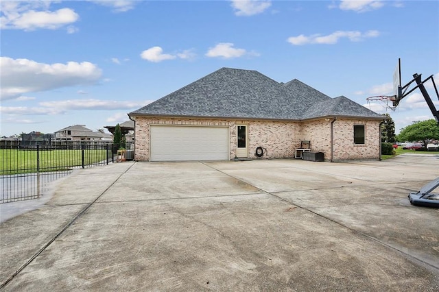 view of home's exterior with a garage, fence, brick siding, a shingled roof, and driveway