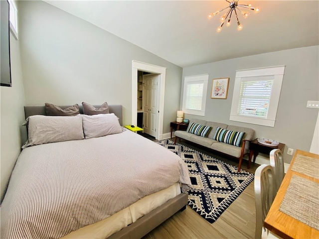 bedroom with baseboards, an inviting chandelier, wood finished floors, and vaulted ceiling